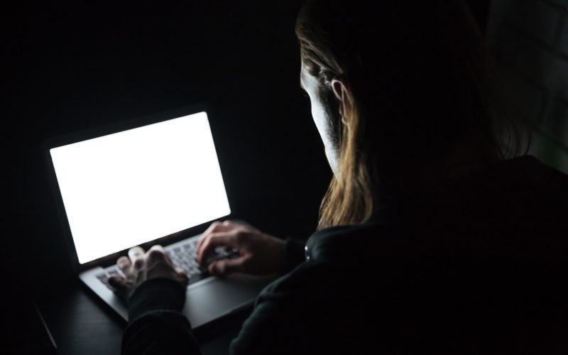 Image of young man using laptop computer at home indoors at night. Looking at laptop display.